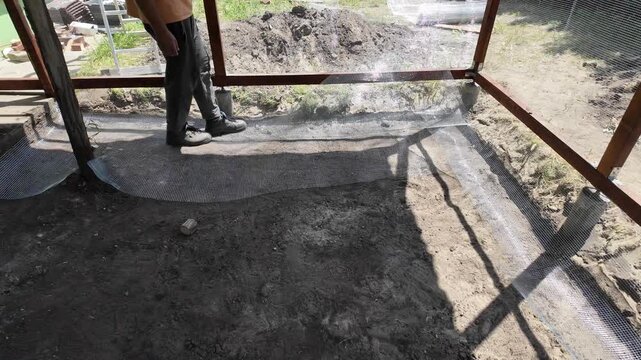A male worker casually laying metal net on the ground with his feet.