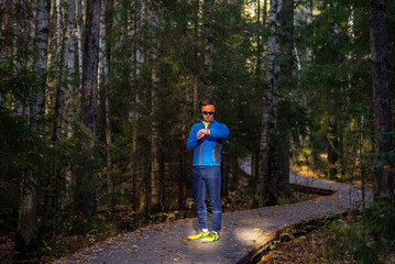 Fototapeta premium Man in athletic apparel is checking his smart watch after a training session on a wooden boardwalk trail surrounded by a dense forest, focusing on health and fitness data in nature