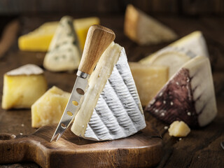 Brie cheese and assorted cheese plate on rustic wooden board.