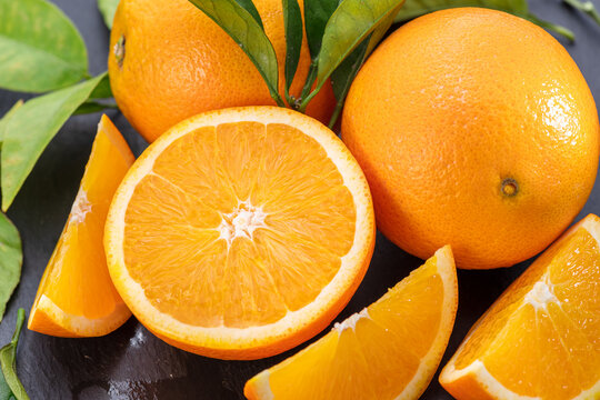 Ripe orange fruits with slices and orange tree leaves on a gray stone table.