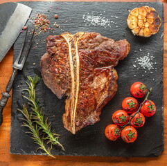 Grilled T-bone steak with seasonings on slate serving plate. Flat lay.