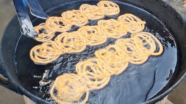An Pakistani shopkeeper at mela or rural fair frying sweets jalebi in oil. Jalebi is a Pakistani dessert. Sweet with sugar syrup fried in oil or ghee. Fresh batch of Jalebi. Jalebis arranged for sale.