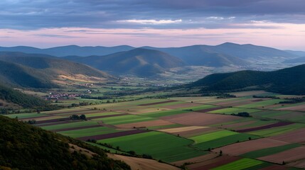 Expansive rural valley panorama at dusk showcasing vibrant patchwork farmland with rolling hills and mountains under a twilight sky