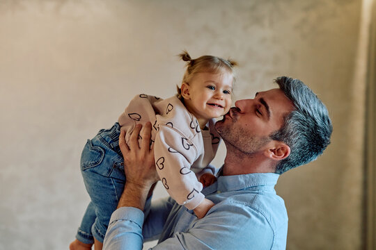 Happy father holding and kissing baby daughter on cheek, expressing love and affection. Family bonding and joy
