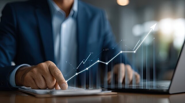 A person is focused on typing and reviewing financial reports on a laptop, with charts and a calculator nearby in a well-lit workspace - Powered by Adobe