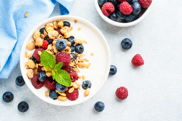 Yogurt with fresh berries and granola on white table.