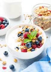 Yogurt with fresh berries and granola on white table.