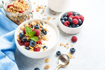 Yogurt with fresh berries and granola on white table.