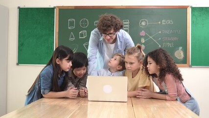 Caucasian teacher and diverse student looking at laptop at classroom. Cute multicultural children learning about coding program or generated program by using software while teacher teaching. Pedagogy. - Powered by Adobe