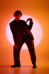 Stylish young man poses dramatically against a vibrant orange backdrop at sunset
