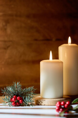 Cozy Christmas still life with two burning white candles, pine branches, and red holly berries