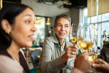 Mature woman toasting with adult friends at a restaurant, happy