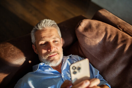 Mature man content using smartphone on sofa at home - Powered by Adobe