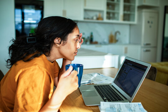 Young adult woman reviewing bills on laptop at home, focused