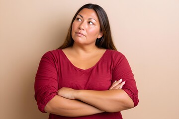 Obraz premium Confident plus size Latina woman with long hair, wearing a red shirt, poses thoughtfully against a neutral background, showcasing natural beauty and self-assurance