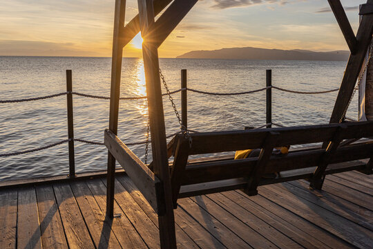 Golden sunset over the calm sea, a wooden pier and swing create with a yellow rucksack a peaceful, relaxing scene perfect for travel, leisure, and seaside lifestyle albums.