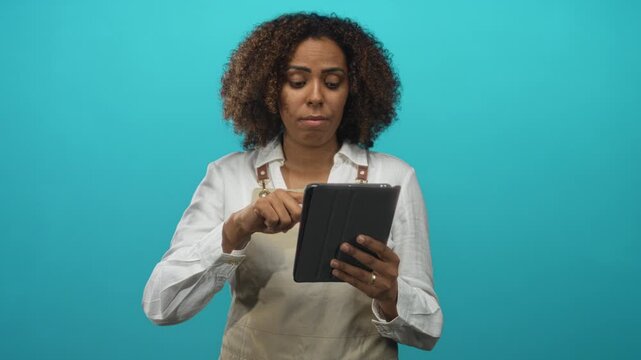 Young african american woman baker wearing apron taps black tablet with right finger in teal studio; focus business planning.
