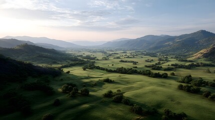 Obraz premium Panoramic view of a lush green valley with rolling hills and scattered trees bathed in soft morning light