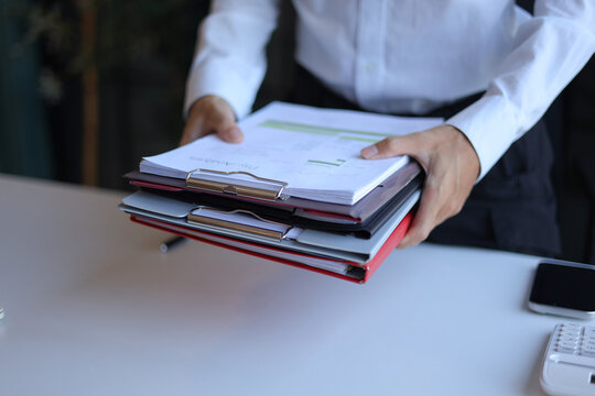 Businessman working in office carrying stack of documents.