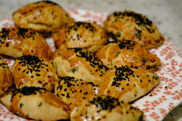 Macro and close-up shot of delicious homemade black cumin pastries. Turkish pastries. Breakfast pastries with cheese and parsley, made by a housewife, on a red plate. Traditional delicacies.