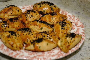 Macro and close-up shot of delicious homemade black cumin pastries. Turkish pastries. Breakfast pastries with cheese and parsley, made by a housewife, on a red plate. Traditional delicacies.
