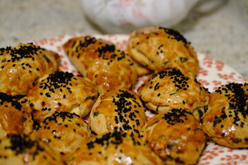 Macro and close-up shot of delicious homemade black cumin pastries. Turkish pastries. Breakfast pastries with cheese and parsley, made by a housewife, on a red plate. Traditional delicacies.