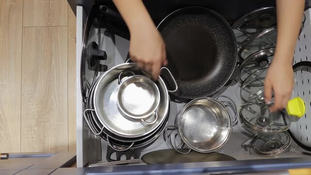Handheld top-down shot of teenager organizing pots and utensils in kitchen drawer showing everyday home routine and tidiness