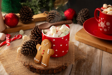 Hot chocolate with marshmallows, a traditional hot drink made for Christmas time and holidays. Served in a red mug and accompanied by gingerbread men cookies.