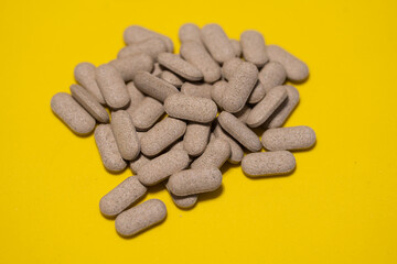 Gray herbal pills on a yellow background. Natural dietary supplement made from plant extracts. Close-up image showing organic medicine or herbal capsules for alternative health and wellness concepts