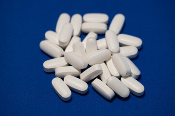 White magnesium tablets on a blue background. Close-up image showing round white pills scattered on a bright blue surface. Concept of health care, dietary supplements, and mineral balance.
