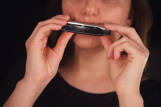 Woman playing harmonica with concentration. Music lessons and hobby concept. Entertainment background on a dark setting with performer enjoying her leisure. - Powered by Adobe