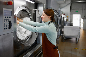 Female worker is loading various clothes into a washing machine