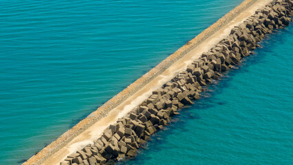Aerial view of a pier with breakwaters separating the turquoise sea.