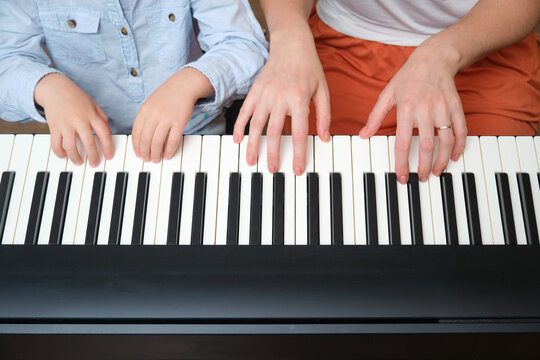 Woman teaches a boy to play the piano. Mother and kid learning music together at home. Family hobby and childhood education concept. A child aged 4 years (four years old)