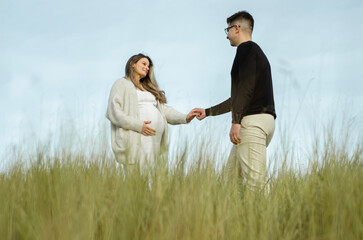 marido e mulher gr&aacute;vida de m&atilde;os dadas, trocando carinho e la&ccedil;os de afeto