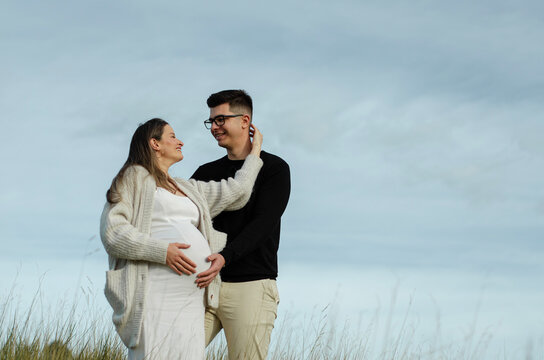 m&atilde;e gr&aacute;vida fazendo carinho no rosto do marido, pai com a m&atilde;o na barriga de gestante