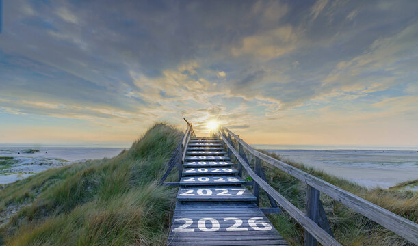 Text 2026, 2027 up to 2035 written on wooden stairway leading over coastal dunes towards sunrise, symbol path into future. Stairway into future, timeline path through coastal dunes. Amrum 2026.