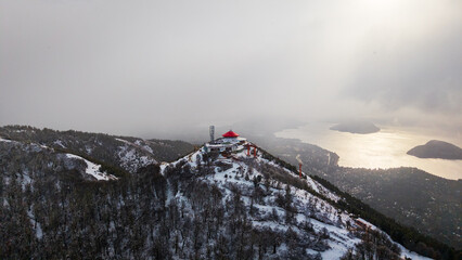 Snowy Cerro Otto refuge with dramatic lake, islands and misty sky, aerial view in Bariloche, Argentina.