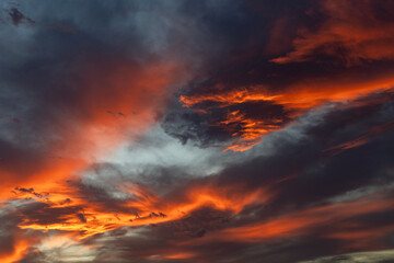 Fototapeta premium Dramatic fiery sunset sky with vibrant red, orange, and dark clouds creating a stunning, atmospheric scene. Beautiful evening sky background with vivid colors and moody contrast.