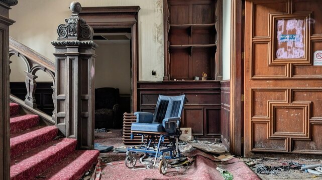 Derelict deserted nursing home interior, abandoned empty wheelchair, ornate staircase. Old vandalised, dusty, run down hall entrance steps. Natural disaster aftermath debris. Disabled neglect, stairs