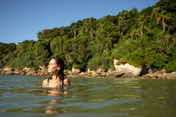 Fototapeta premium Woman enjoying a peaceful moment in the calm waters near a lush tropical coastline at midday