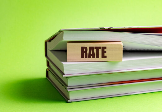 Wooden block with the word rate placed between stacked books on green background - Powered by Adobe