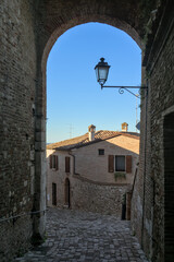 Cobblestone alleyway in Santarcangelo di Romagna, Italy, framed by an archway and brick houses.