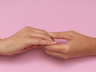 Closeup of woman holding her own hands on pink background. Hands together.