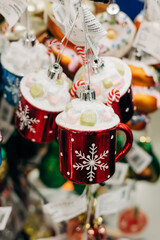 Decorative holiday ornaments shaped like red mugs with whipped cream and candy canes hanging in festive display
