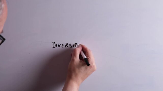 An HR business professional is writing Diversity and Inclusion on a whiteboard in black marker pen, ideal for DEI, HR, recruitment, and business workplace presentations.