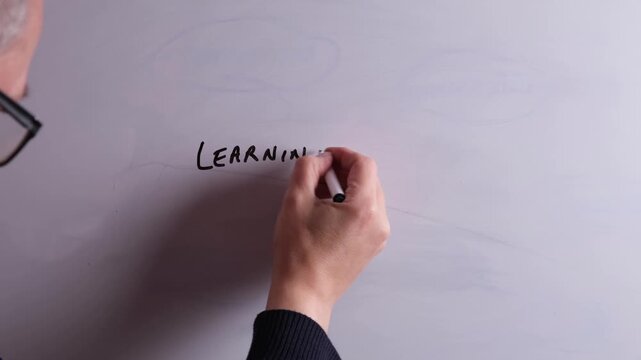 An HR business professional is writing Learning and Development on a whiteboard in black marker pen, ideal for HR, recruitment, and business workplace presentations.