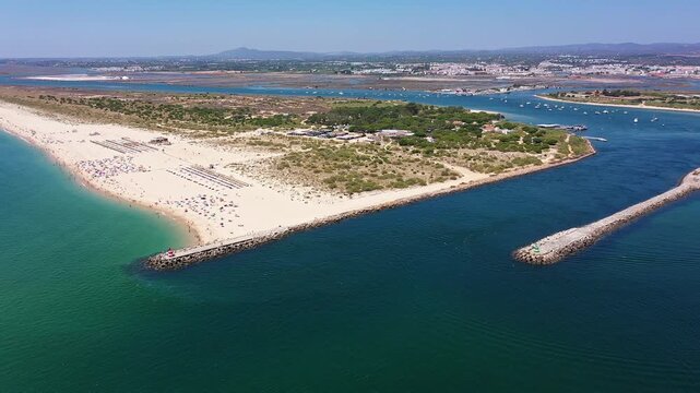 Aerial view drone shot of Tavira Portugal Algarve dramatic aerial of coastal spit and channel into ria formosa, boats navigating inlet and visitors on sunlit beach coastal engineer