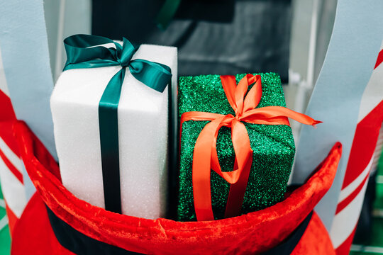 Brightly wrapped gifts with colorful ribbons sit in a festive red sack during a holiday celebration