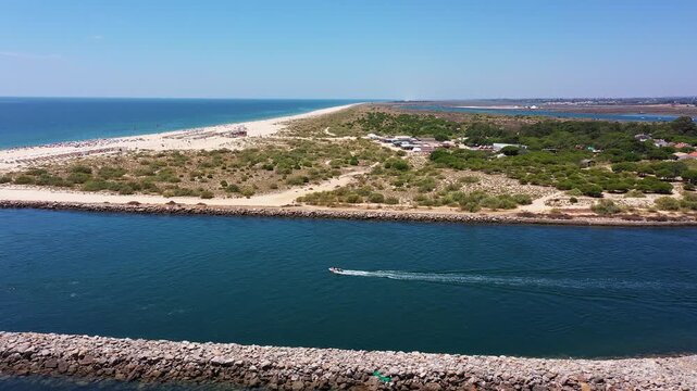 calm ria formosa channel with boat cruising along protected inlet captain steering wake past rocky breakwater marina and sand spit visible, clear blue water reflecting sky and distant Portugal Tavira